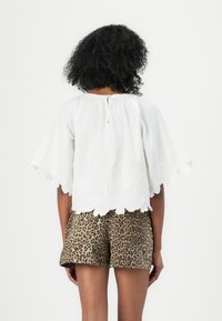 Haut en coton blanc avec un ourlet festonné et une broderie florale, associé à un short en imprimé léopard brun. Coupe légère et décontractée avec un col rond.