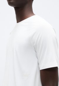 Άσπρο αθλητικό t-shirt με κοντά μανίκια, λεία υφή, αδιάκοπο σχέδιο και μικρή ανάγλυφη λεπτομέρεια λογότυπου στο στήθος.