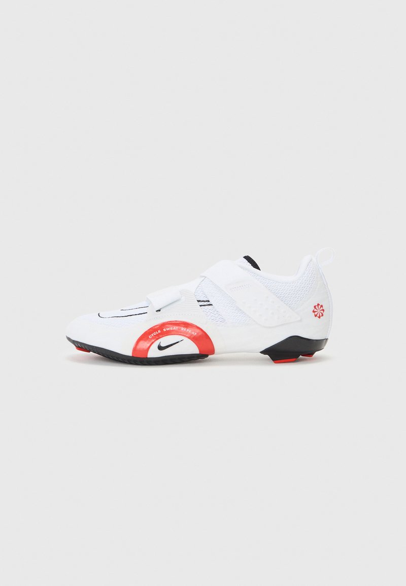 Scarpa sportiva bianca con tomaia in rete, accenti rossi e neri, una fascia in velcro e suola testurizzata. Presenta il marchio vicino al tallone e alla punta.