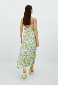 Robe midi florale avec bretelles spaghetti réglables, dans des couleurs pastel sur un fond jaune clair, présentant un design à dos nu.