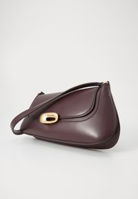 Sac à main en cuir bourgogne foncé avec une forme asymétrique, quincaillerie dorée et une seule sangle pour l'épaule. Présente des détails cousus.