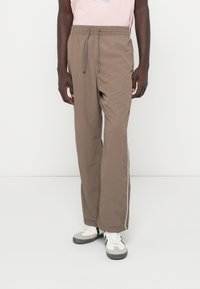 Καφέ ελαφριά joggers με ελαστική μέση και κορδόνι. Διαθέτει λευκές πλαϊνές ρίγες και χαλαρή εφαρμογή, κατασκευασμένα από μαλακό ύφασμα.