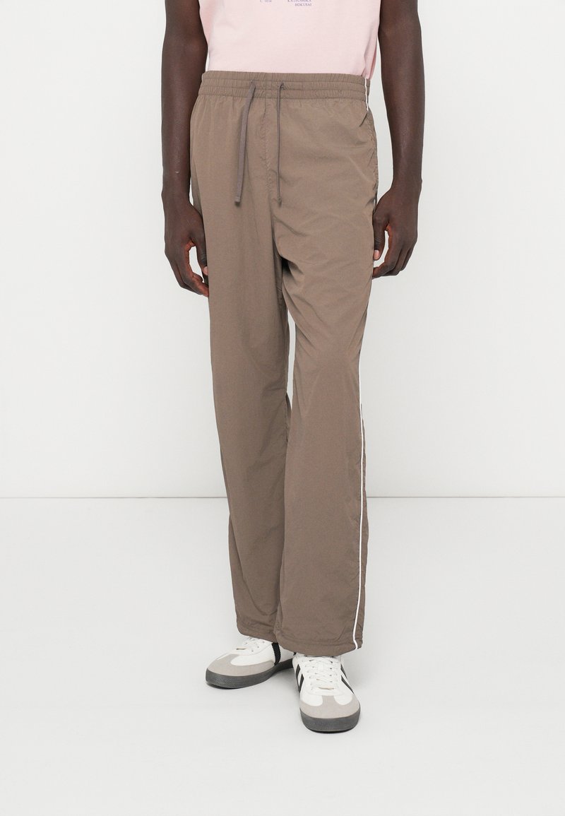 Καφέ ελαφριά joggers με ελαστική μέση και κορδόνι. Διαθέτει λευκές πλαϊνές ρίγες και χαλαρή εφαρμογή, κατασκευασμένα από μαλακό ύφασμα.