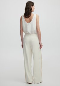 White satin tank top with a low back, paired with high-waisted, wide-leg pants in cream, featuring side slits and back pockets.