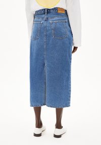 Falda midi de mezclilla en azul claro, con corte recto, bolsillos traseros y una abertura central. Presenta una etiqueta de cuero con la marca en la cintura.