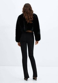 Sort faux fur kort jakke med brede ærmer, parret med slim-fit sorte bukser og højhælede sko, set fra ryggen.