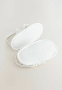 Bílé látkové sandály s texturovaným svrškem, měkkým podšívkou a hladkými podrážkami. Zaoblený tvar s jemným zdobením podél popruhů.