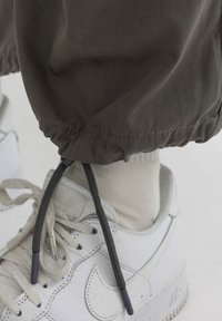 Grijze broek met trekkoord en elastische boorden, gecombineerd met witte leren sneakers en lichtbeige sokken, met zwart getipte veters.
