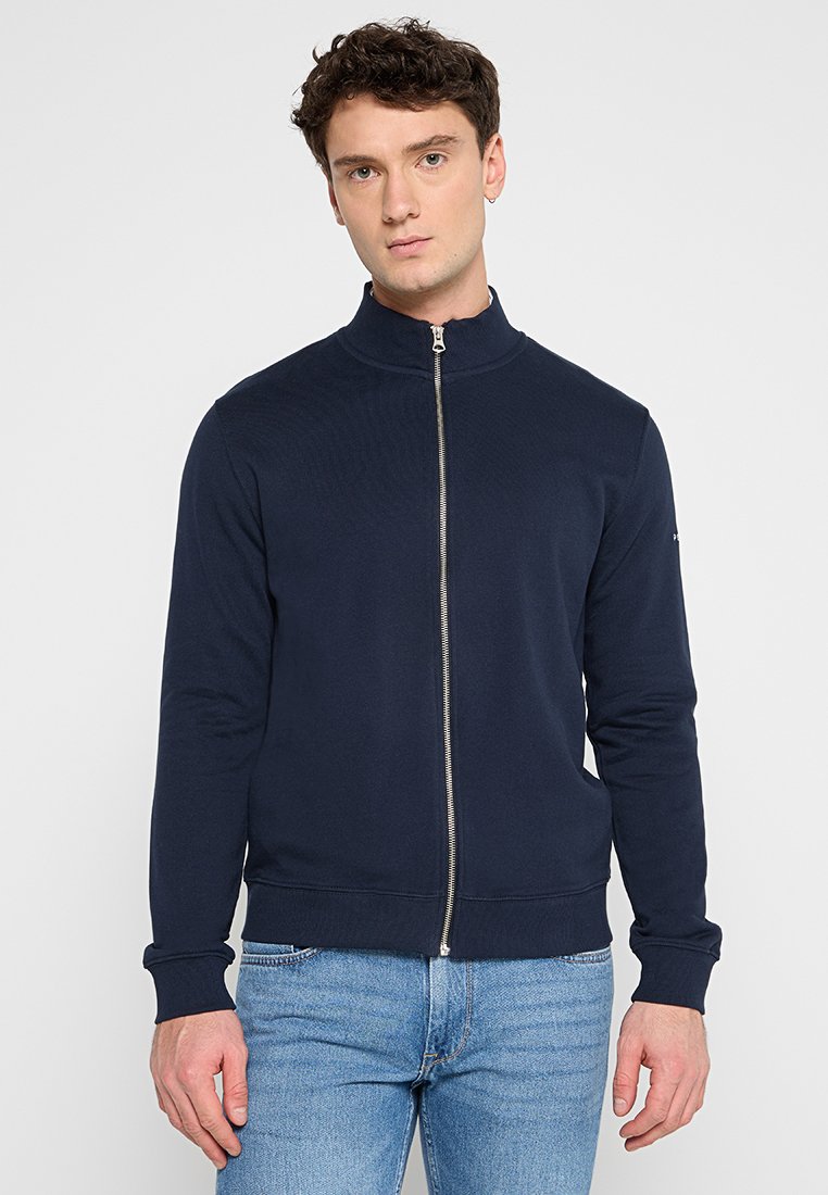 Marineblauer Reißverschlussjacke mit hohem Kragen, aus einem weichen Stoff gefertigt. Verfügt über gerippte Bündchen und Saum, mit einem minimalistischen Design und silbernem Reißverschluss.