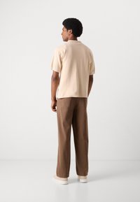 Beige kortærmet skjorte med subtil tekstur, parret med løse brune bukser. Sættet afsluttes med cremefarvede sneakers.