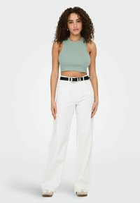 Muntgroene geribbelde crop top met een ronde halslijn, gecombineerd met witte wijde broek en een zwarte riem. De schoenen zijn crème van kleur met een dikke zool.
