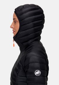 Profil af en person iført en sort quiltet hættetrøje med en orange lynlås og et mammut-logo på ærmet.