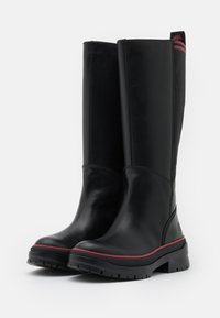 Bottes noires en cuir montantes jusqu'aux genoux avec une finition lisse, dotées d'une semelle en caoutchouc, d'accents roses sur le bord et d'un tissu noir texturé à l'arrière.