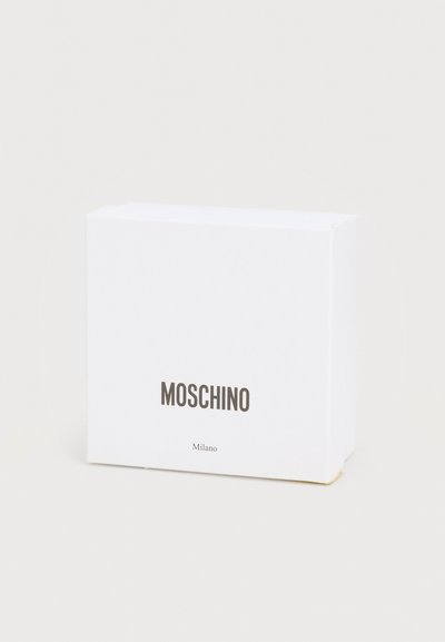 Λευκό ορθογώνιο κουτί με τη λέξη "MOSCHINO" σε έντονα μαύρα γράμματα και τη λέξη "Milano" σε μικρότερη γραμματοσειρά από κάτω, πάνω σε απλό ανοιχτόχρωμο φόντο.