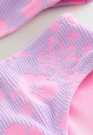 Light pink fabric features a textured lavender pattern of flowers and leaves. The design showcases a soft, knit-like texture interwoven with smooth areas.