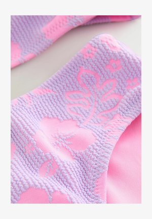 Gaiši rozā audums ir dekorēts ar teksturētu lavandas ziedu un lapu rakstu. Dizains izceļ mīkstu, adīšanas līdzīgu tekstūru, kas mijas ar gludām virsmām.