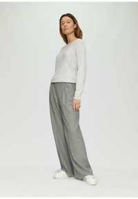 Hellgrauer, gerippter Strickpullover mit langen Ärmeln, kombiniert mit weit geschnittenen grauen Hosen und weißen Sneakers. Minimalistisches Design und Textur.