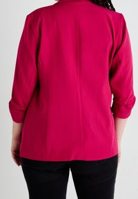 Rosa skräddarsydd kavaj med trekvartsärmar, bakseams och en mjuk textur. Matchad med mörka jeans för kontrast.