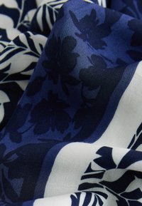 Marineblauwe stof met witte bloemenpatronen. De textuur lijkt glad, met contrasterende donkere silhoetten en een vloeiende vormgeving.