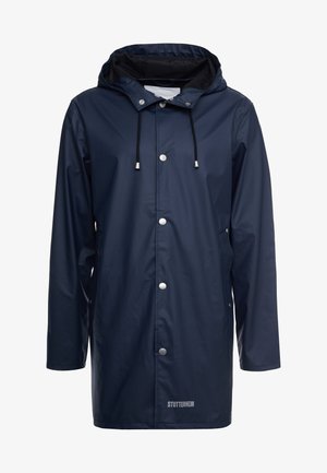 Marin vattentät regnjacka med huva, tryckknappar och dragsnodd. Har en slät, glänsande yta och en logotyp vid fållen.