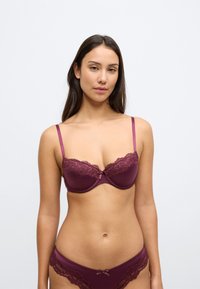 Bordó csipkés melltartó puha párnázással, vékony állítható pántokkal és egy masni díszítéssel a közepén. Hozzáillő csipkés bugyival stílusosan párosítva.