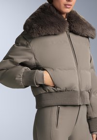 Párnázott bomberdzseki tompa taupe színben, puha szürke szőrme gallérral. Bordázott mandzsetták és szegély, cipzáras lezárás, oldalsó zsebekkel. Sima textúra.