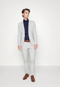 Light gray suit with tailored fit, navy button-up shirt, brown leather belt, and matching brown dress shoes. Smooth fabric and modern design.