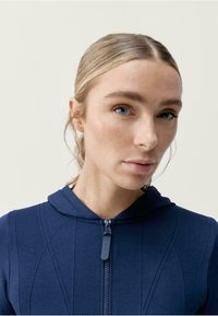 Jūras spēku krāsas zip-up kapuce ar teksturētu, ribotu dizainu un kapuci, ar priekšējo rāvējslēdzēju un izsmalcinātām akcenta detaļām.