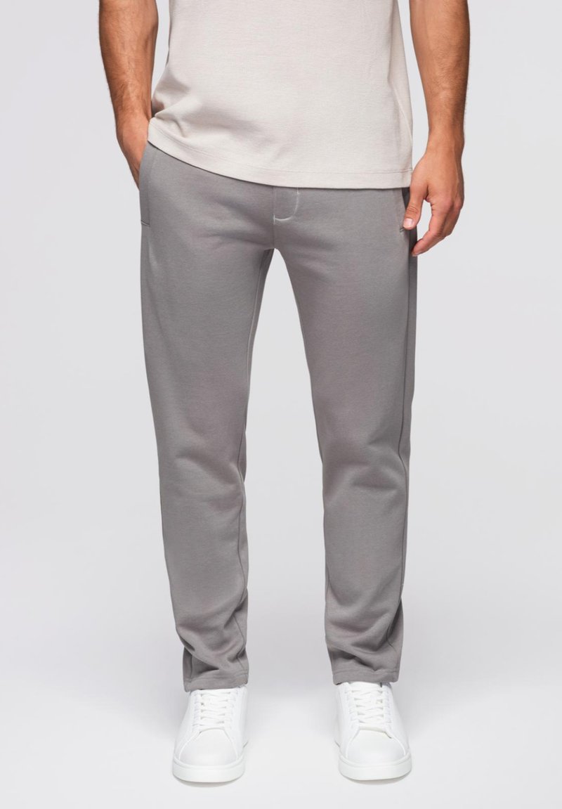 Grijze sweatpants van zacht materiaal, taps toelopend design, elastische tailleband, zijzakken, gecombineerd met witte sneakers voor een casual look.