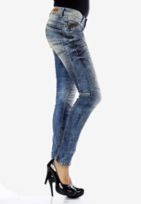 Jean slim en denim bleu délavé avec des coutures délicates, de multiples poches et une coupe contemporaine, associés à des talons hauts noirs.