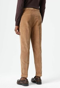 Brown corduroy trousers displayed from the back, featuring a straight fit, rolled cuffs, two rear pockets, and a textured finish.