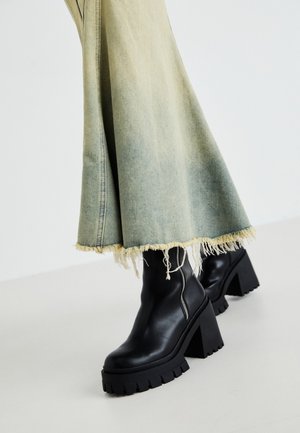 Melnas ādas potītes zābaki ar masīvu faktūru zoli, kopā ar izbalējušu džinsa svārku ar saplēstiem galiem. Sānos ir rāvējslēdzēja detaļa.