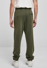 Olivengrønne joggebukser med elastisk midje, oppbrettede hem og en baklomme. Kombinert med hvite sneakers med grønne logo-detaler.