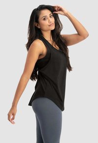 Schwarzes, ärmelloses Tanktop mit lässiger Passform, abgerundetem Saum und weicher Textur, kombiniert mit grauen Leggings. Minimales Design, keine Muster oder Hardware.