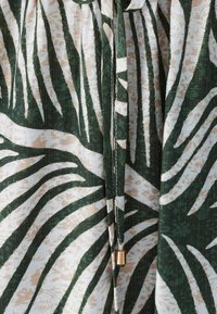 Roheline ja valgekattega tekstiil, millel on troopiliste lehtede muster. Sisaldab metallilise aktsendiga nööri. Kerge ja tekstuuriga kangas.