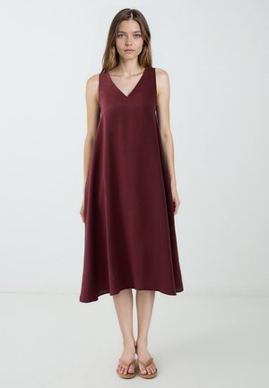 Maroon ärmelloses Kleid mit V-Ausschnitt, fließender Silhouette, glattem Stoff und knielangem Saum. Getragen mit braunen Sandalen.