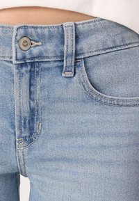 Jeans de denim azul claro con cintura alta, presillas para cinturón, un botón de metal y bolsillos delanteros con detalles de costura sutiles.