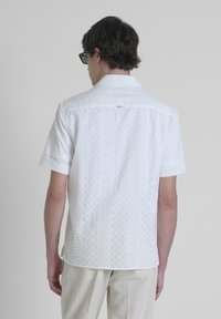 Camicia bianca a maniche corte con un motivo a diamante testurizzato, colletto button-down e un piccolo logo vicino al collo.