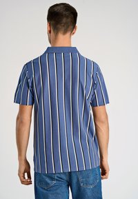 Koszulka polo z krótkim rękawem w kolorze niebieskim w białe paseczki, z klasycznym kołnierzykiem i luźnym krojem. Widok z tyłu pokazuje wzór w pionowe paski.