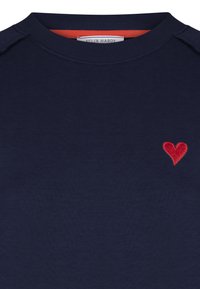 Mörkblå crewneck sweatshirt med ett litet rött broderat hjärta på vänster bröst och synlig Felix Hardy-etikett inuti kragen.