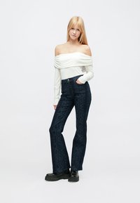 Off-the-shoulder white top with long sleeves, paired with dark blue flared jeans featuring a textured snake pattern and black platform boots.