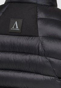 Sort puffervest med quiltet tekstur, mat stof og en rektangulær logo-patch med navnet "Alessandro" i sølv.