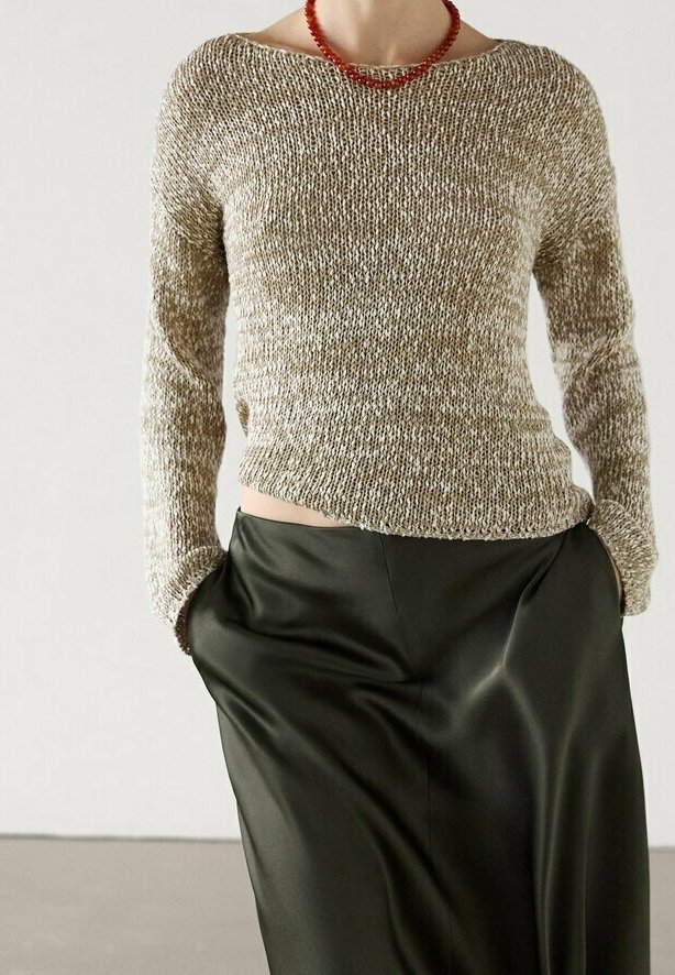 Pull en tricot beige et crème, avec un large décolleté et des manches longues, assorti à une jupe en satin vert foncé. Collier rouge perlé exposé.