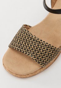 Flettede sandaler med et svart og naturlig fargemønster, korksåle og en semsket fotbed; har en bred rem og minimalistisk ankelrem.