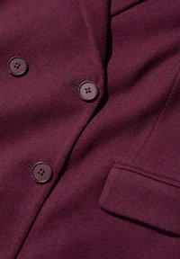 Abrigo de mezcla de lana burdeos con dos botones redondos oscuros y un bolsillo, con una tela texturizada y un diseño clásico de doble botonadura.