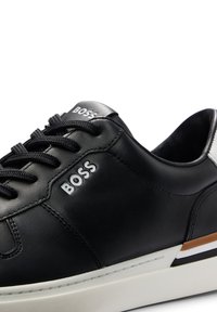 Sneaker in pelle nera con punta rotonda, lacci neri, logo "BOSS" impresso, suola bianca e accentatura a blocchi di colore sul tallone.