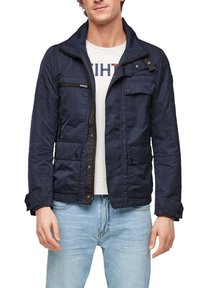 Mörkblå lättviktsjacka med dragkedja framtill, flera fickor och en bröstficka med dragkedja. Har en slät yta och en upprättstående krage.