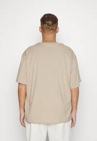 Beige, short-sleeve t-shirt with a loose fit and round neckline, made of soft fabric, depicted from the back against a white background.