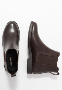 Botas de tobillo de cuero marrón con paneles laterales elásticos, puntera redondeada y un tacón bajo cuadrado, con un acabado texturizado y una tira de agarre.