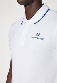 Polo shirt bianco realizzato in tessuto testurizzato, con strisce di accento blu sul colletto e logo ricamato sul petto.